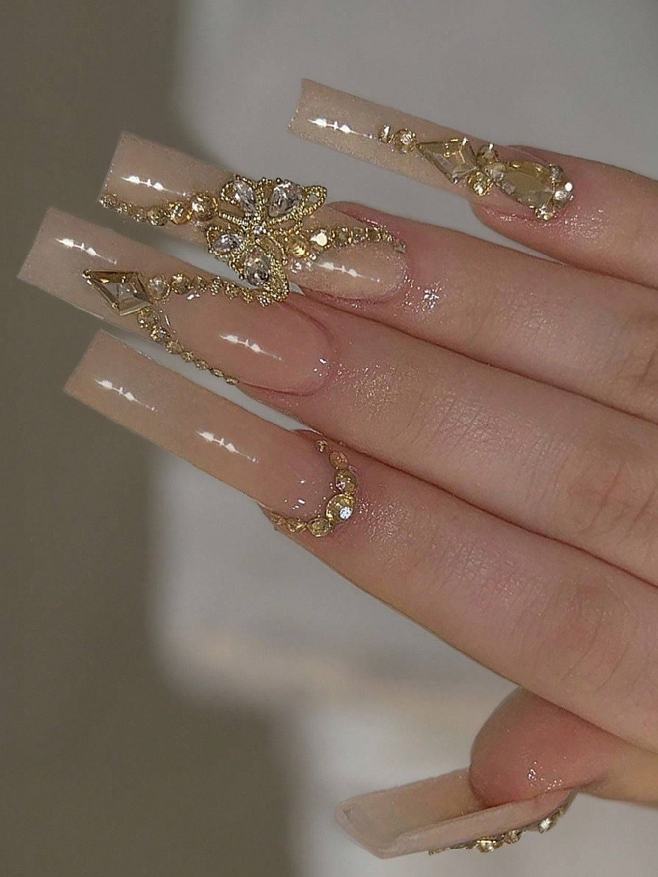 Elegant 24-piece XL square press-on nails in a nude shade with intricate gold embellishments and rhinestone accents for a luxurious manicure look.