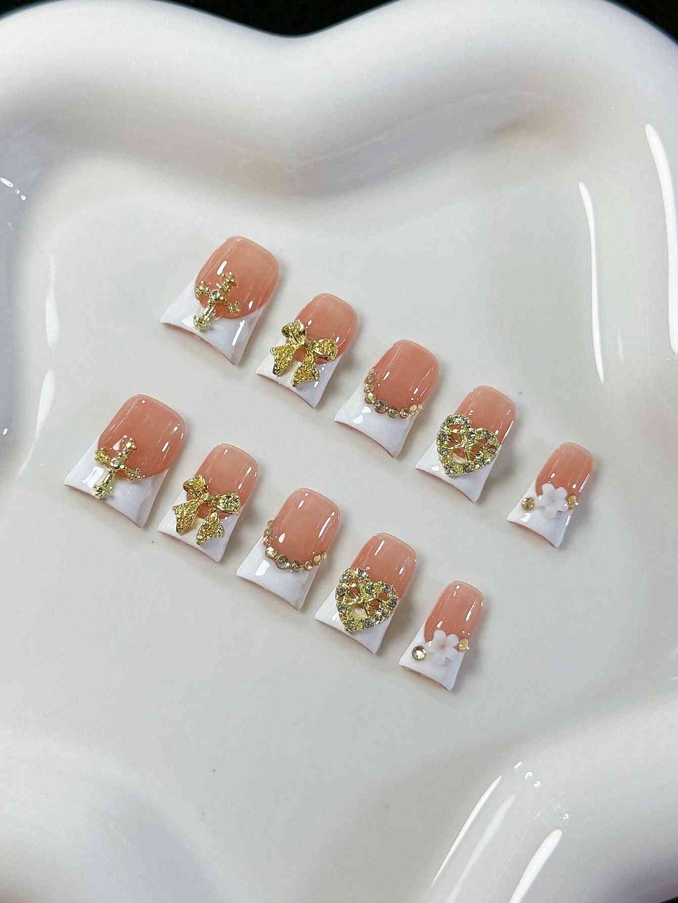 Elegant white French oval fake nails with gold embellishments, featuring intricate bows, hearts, and pearl accents. A luxury 10-piece press-on nail set.