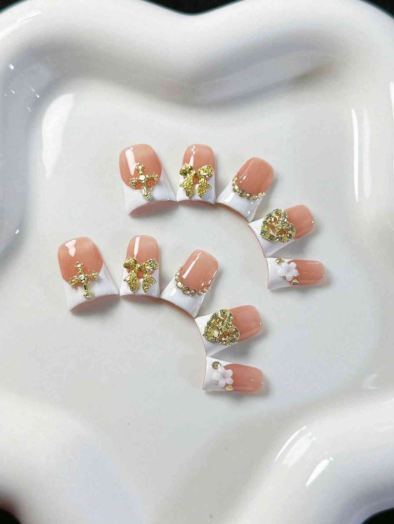 Elegant white French oval fake nails with gold embellishments, featuring intricate bows, hearts, and pearl accents. A luxury 10-piece press-on nail set.