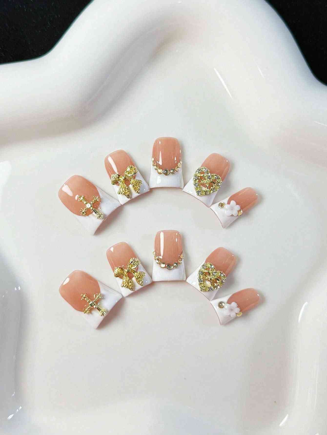 Elegant white French oval fake nails with gold embellishments, featuring intricate bows, hearts, and pearl accents. A luxury 10-piece press-on nail set.