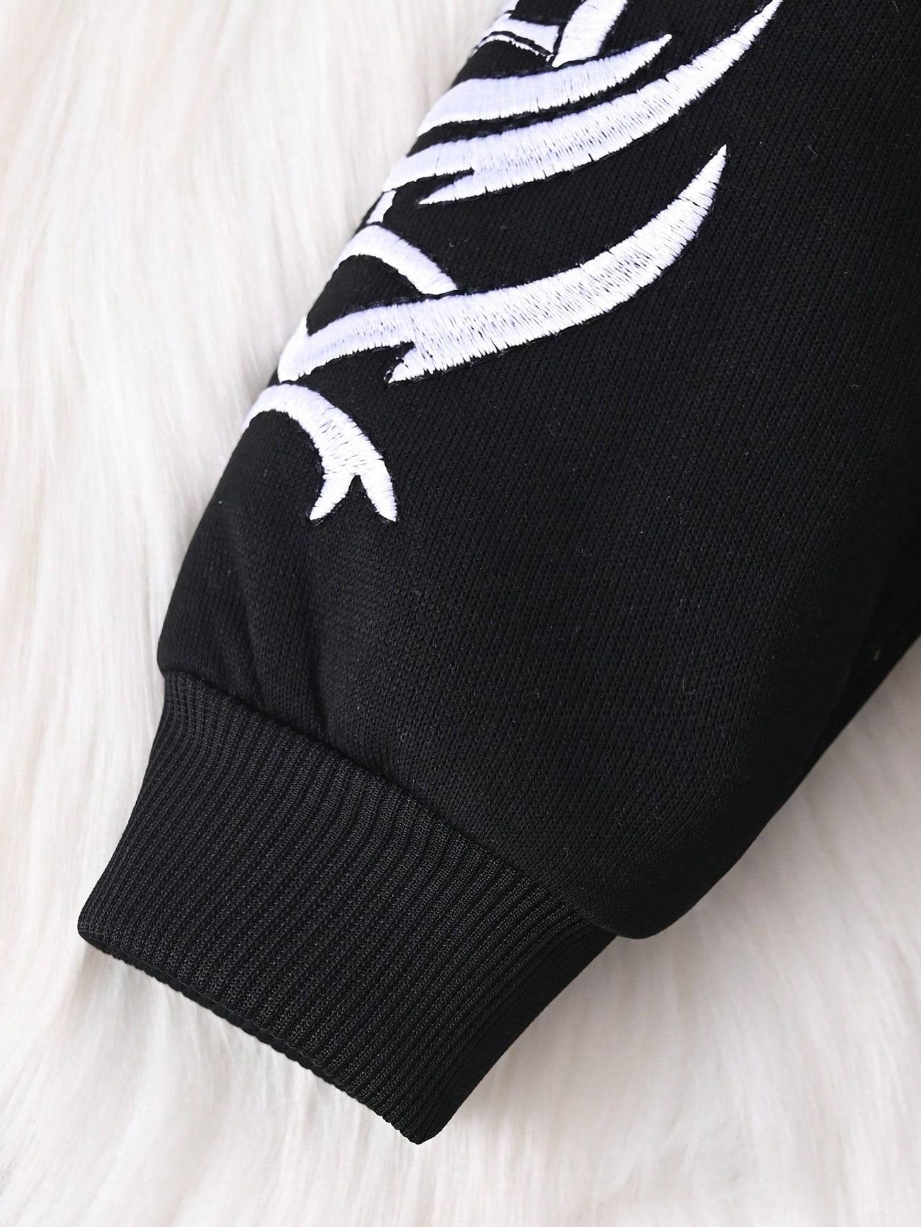 Close-up of sleeve cuff on black hoodie with white embroidered design, highlighting the fine stitching and ribbed detail.